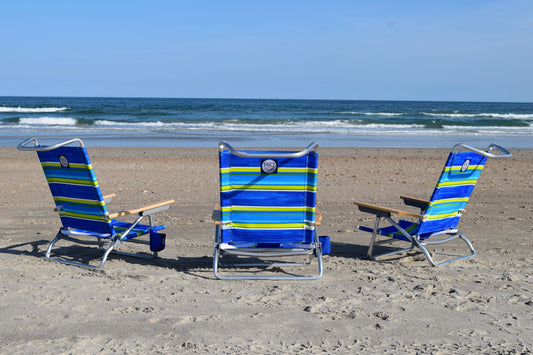 Three foldable beach chairs with blue and yellow stripes, arranged on a sandy beach with the ocean in the background.