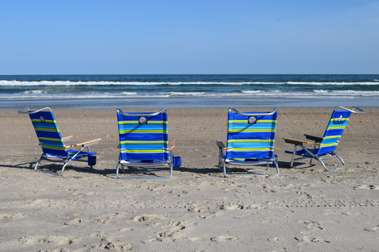 A set of four foldable beach chairs with blue and yellow stripes, arranged on a beach near the ocean.