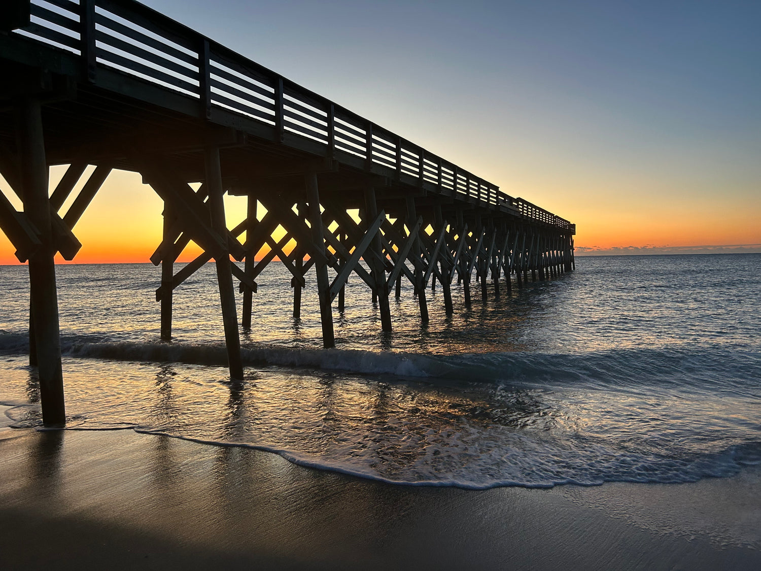 Long wooden pier extending into the ocean at sunset.