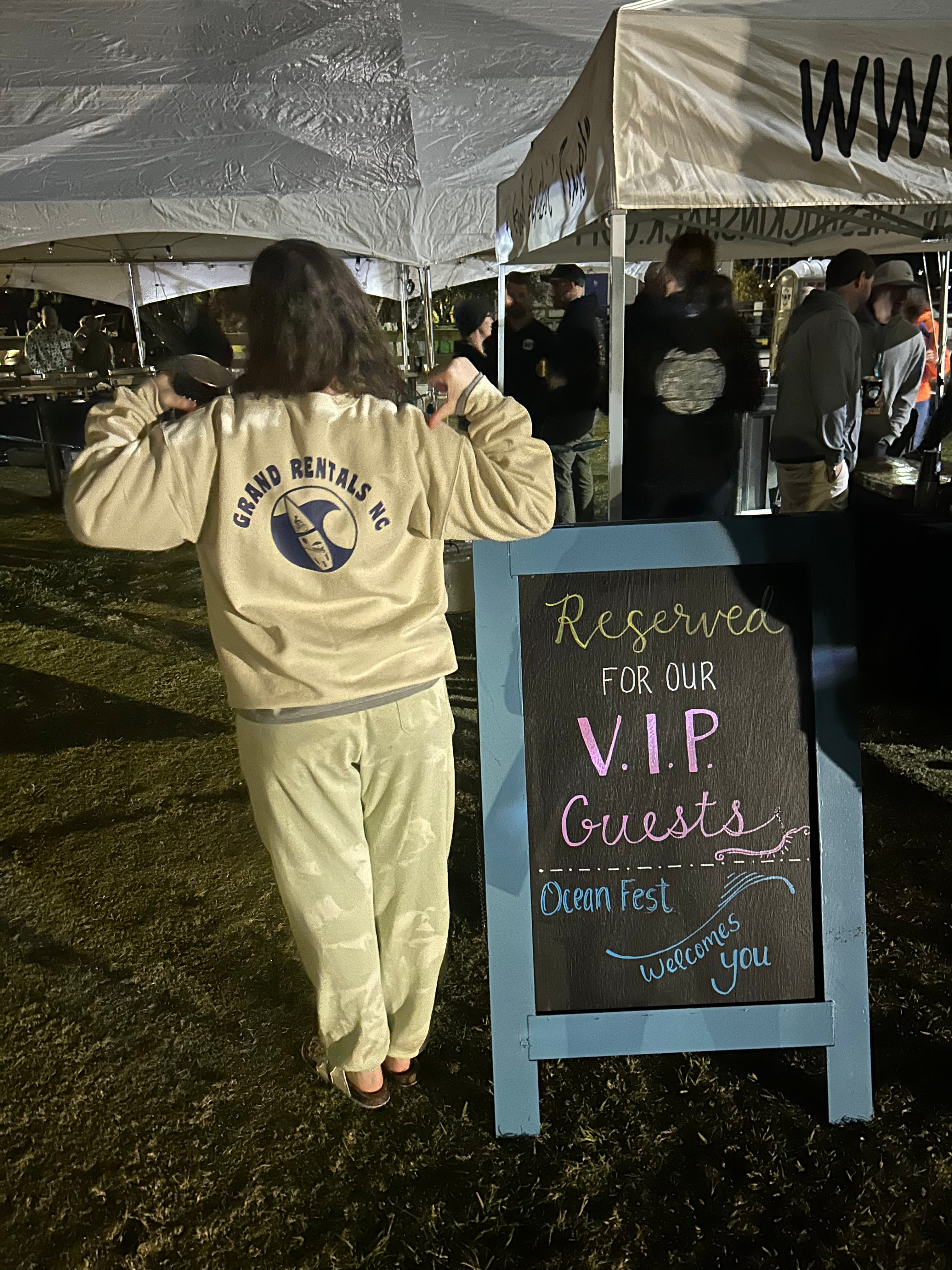Person in a beige Grand Rentals NC tracksuit standing next to a sign reserved for VIP guests at an event. 